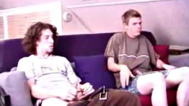 Adam and Christian sit next to each other on the couch watching a porno. They unzip and stoke for a bit, before taking turns sucking each other's hard cock.