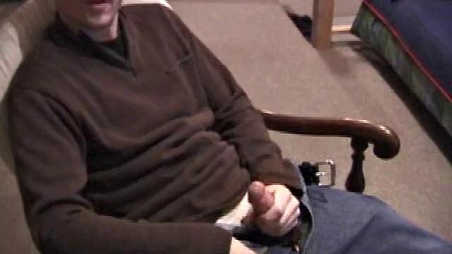 By the time the camera finds him, Dan is already going for his woody. He seems uncomfortable in the chair, so he stands up and moves to the staircase, where we can see his cock getting harder and harder.