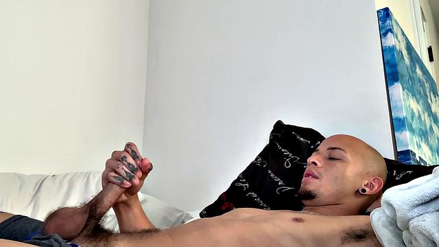 We join Joseph already stripped to his underwear and playing with his package. He reaches in and pulls out his big uncut cock and works up a stiff one. Once completely naked, the inked Latino starts beating off.
