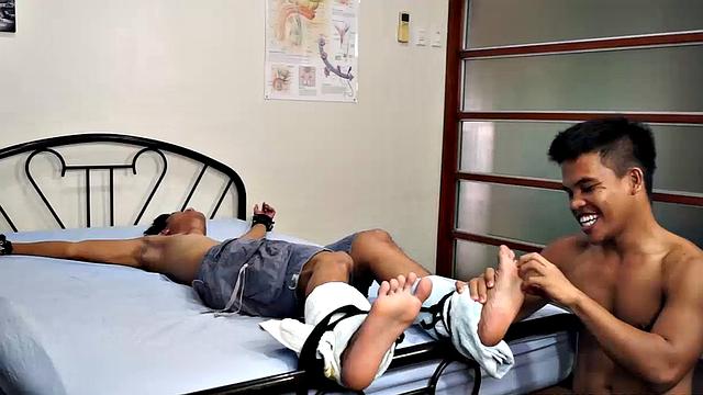 Jacob has his sexy buddy Simon spreadeagled on the bed for some tickling fetish action. Jacob loves tickling so he spends plenty of time on those Asian boy feet. But that's not to say Simon isn't ticklish on his upper body.