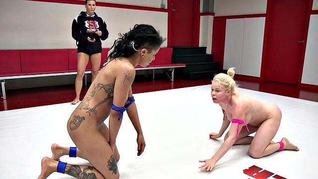 Black inked wrestler fights on mat against white MILF