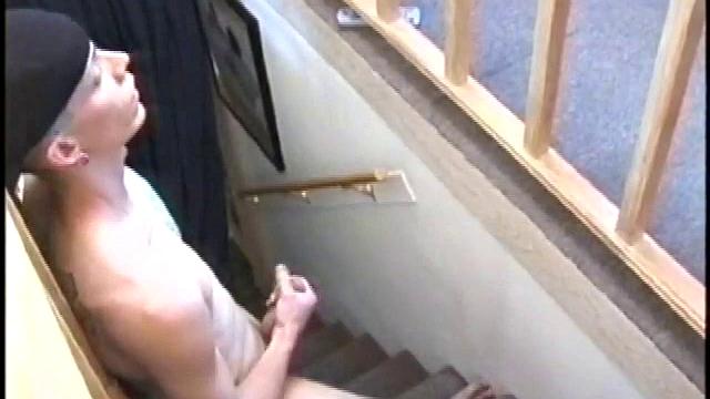 Dressed in baggy shorts and a baseball cap, Shane stands halfway up a short stairway, watching his porn video while talking about making the wall the target for his cum shot.