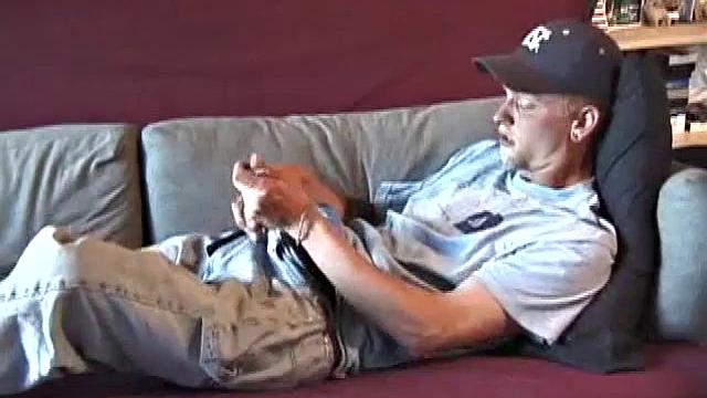 Young amateur Brandon reclines on the sofa and pulls off his pants. Watching porn video, he rubs his dick hard and fingers his asshole.