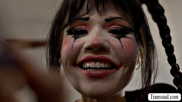 Пышногрудая клоунесса сосёт член своей транс-соседки и даёт ей трахнуть себя в киску, пока та мастурбирует на кровати.