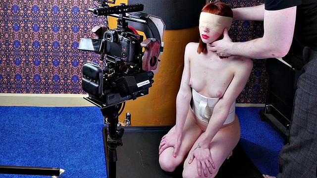 Redhead slavegirl gags on a big cock while blindfolded and tied up in backstage sex-toy action