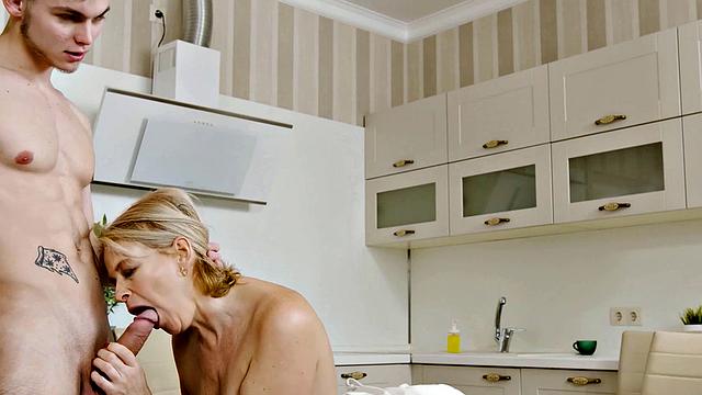 Watch as a young stud bangs the mature blonde next to her husband in the kitchen