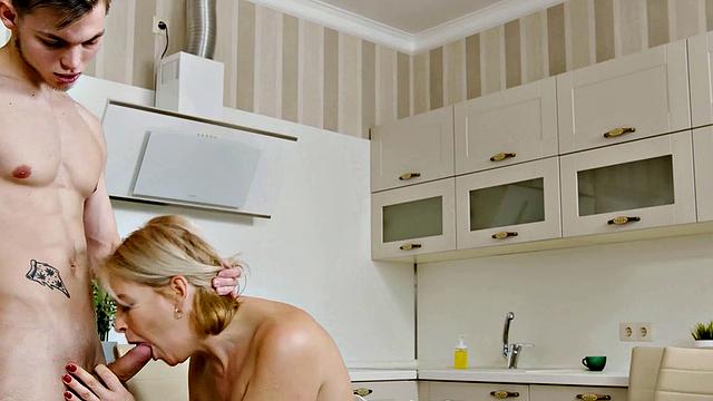 Watch as a young stud bangs the mature blonde next to her husband in the kitchen