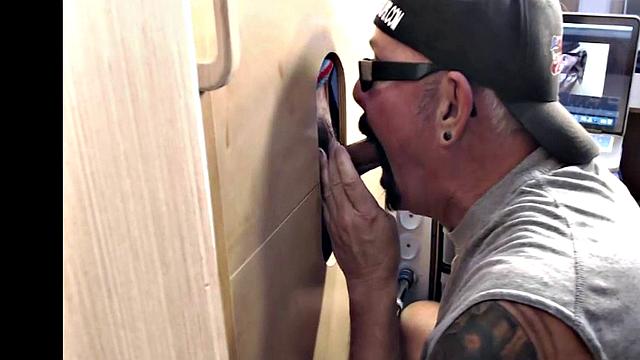 Gloryhole inked DILF sucks BFs cock through hole at home
