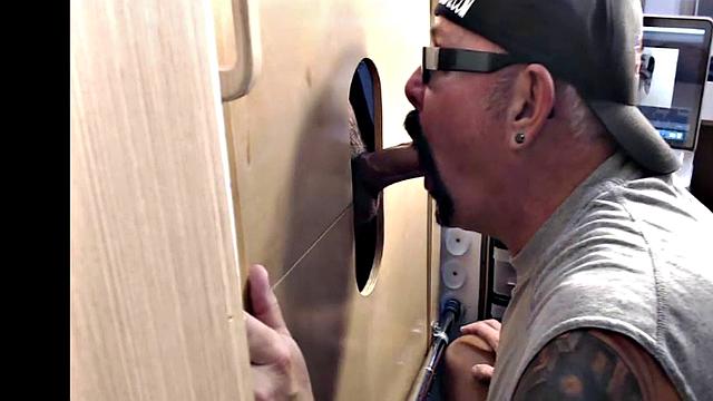Gloryhole inked DILF sucks BFs cock through hole at home