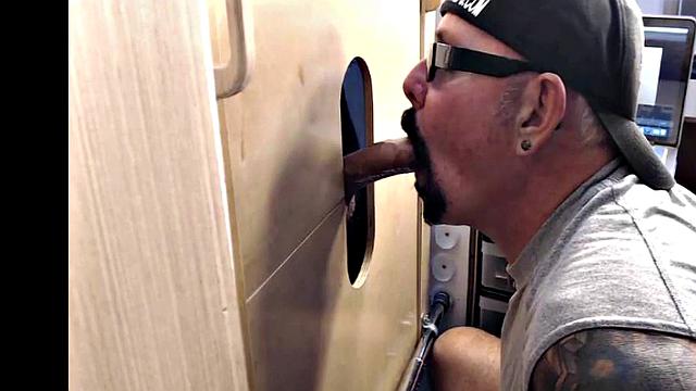 Gloryhole inked DILF sucks BFs cock through hole at home