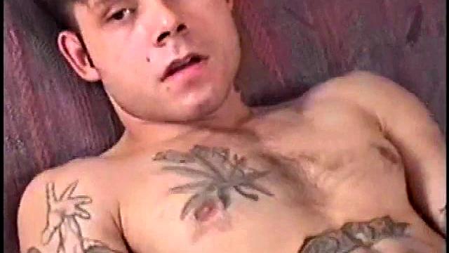 This tattooed misfit quickly strips down, lubes up, and strokes on the sofa.